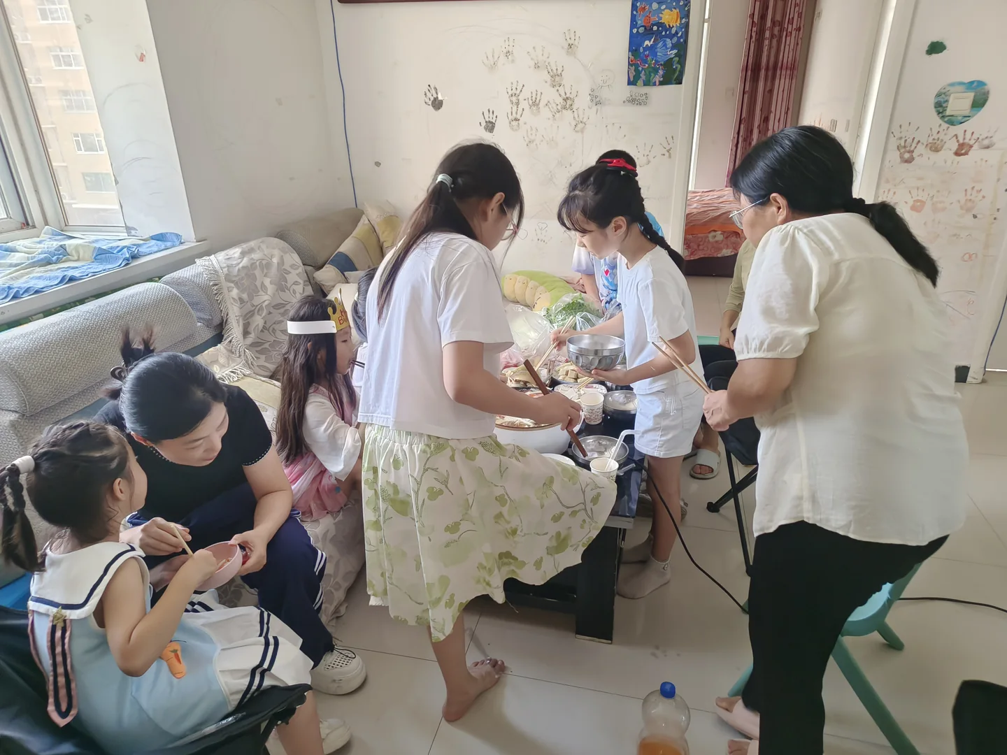 几位大人与孩子围着低桌准备食材，桌面有碗盘和成袋蔬菜
