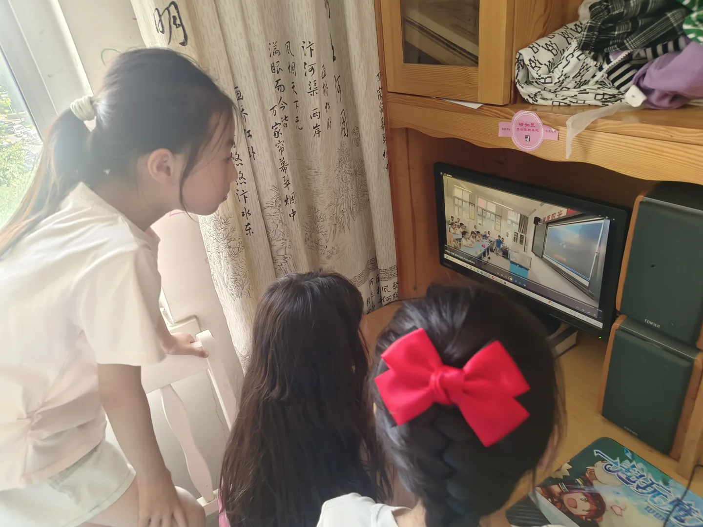 三位孩子站在书桌前看电脑，画面中央可见红色蝴蝶结