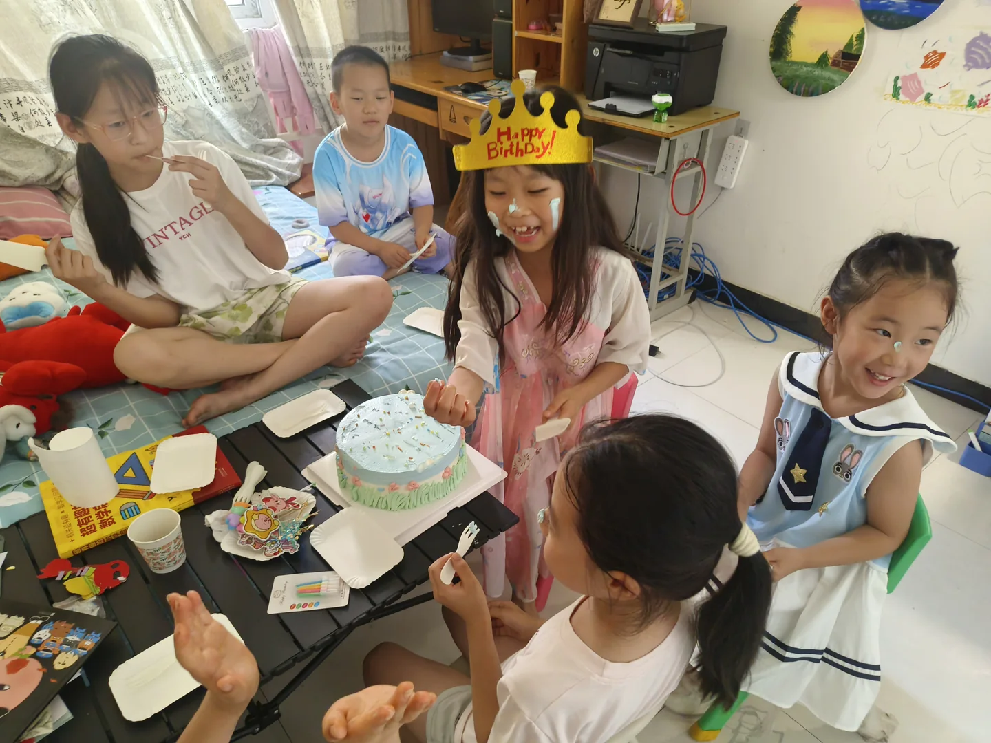 戴黄色生日皇冠的柔柔坐在浅蓝色蛋糕旁，小朋友围在低桌周围
