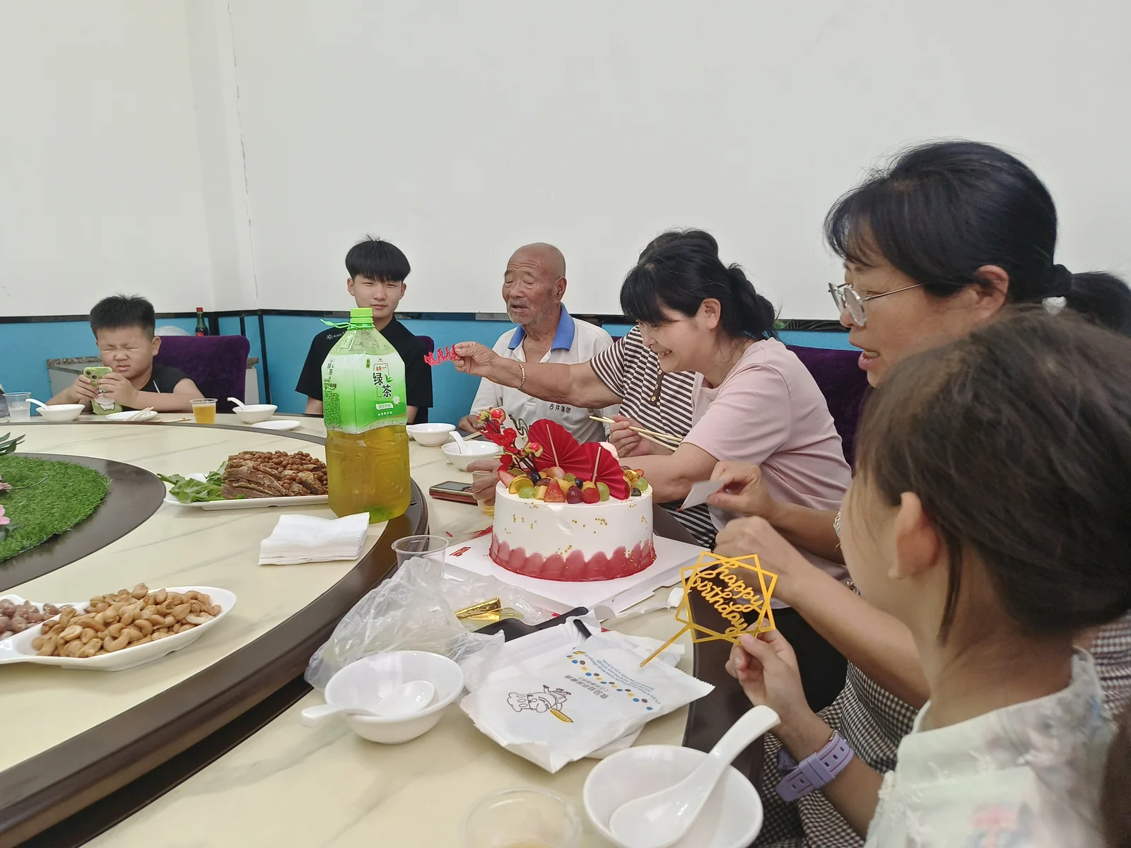 姥爷戴生日冠坐在蛋糕后方，家人围坐