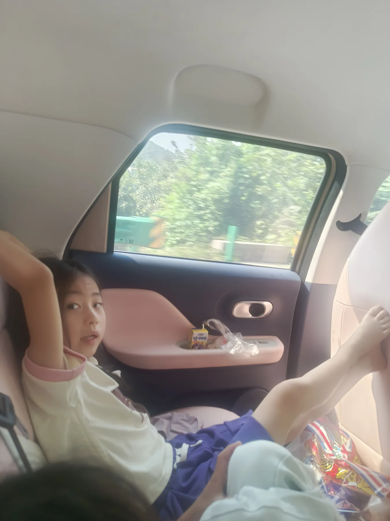 自驾途中坐在车内看向镜头的孩子，窗外已出现绿色山景