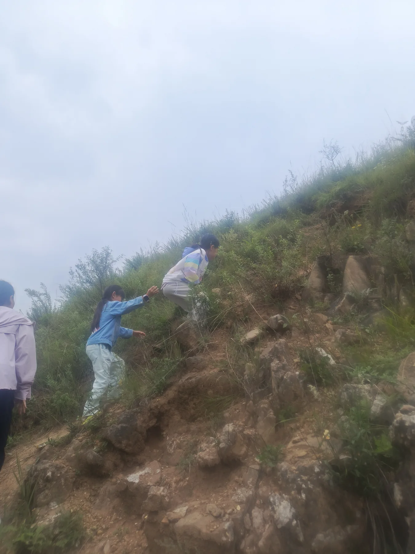 两个孩子一前一后攀爬陡峭山坡并互相照应